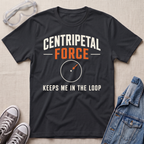 A black graphic t-shirt laid flat on a light beige textured background, styled with safety goggles, gray sneakers, and a denim jacket. The t-shirt features the text 'CENTRIPETAL FORCE KEEPS ME IN THE LOOP' in white and orange lettering with a small circular diagram graphic.