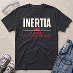 A black graphic t-shirt laid flat on a textured beige background, styled with safety goggles, gray sneakers, and a denim jacket. The t-shirt features the word 'INERTIA' in bold white letters, with a small red block and red text underneath reading 'I'D EXPLAIN IT, BUT I'D RATHER STAY AT REST'.