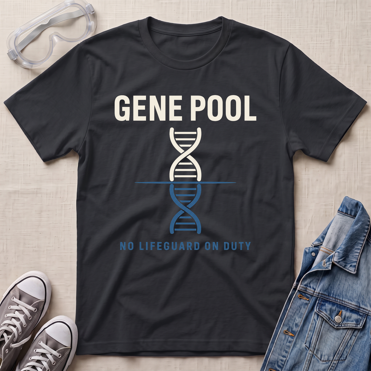 A black graphic t-shirt laid flat on a light beige textured background, surrounded by lifestyle props including safety goggles, gray sneakers, and a denim jacket. The t-shirt features a white and blue DNA double helix graphic with the text 'GENE POOL' and 'NO LIFEGUARD ON DUTY'.