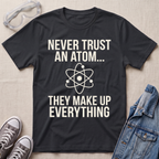 A black graphic t-shirt with white text reading 'NEVER TRUST AN ATOM.' and 'THEY MAKE UP EVERYTHING' with an image of an atom in between the texts.