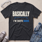 A black graphic t-shirt laid flat on a light beige textured background, styled with safety goggles, gray sneakers, and a denim jacket. The t-shirt features the text 'BASICALLY I'M QUITE BASIC' in white and blue lettering.