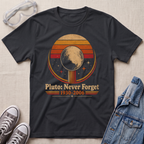 A black graphic t-shirt laid flat on a light beige textured background, styled with clear safety goggles, gray sneakers, and a blue denim jacket. The t-shirt features a retro circular graphic of Pluto with the text 'Pluto: Never Forget 1930-2006'.