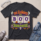 A black graphic t-shirt featuring a Halloween-themed design with the text 'THE ELEMENTS OF BOO SURPRISE' and periodic table elements styled as potion bottles, ghosts, pumpkins, and a skull. The shirt is displayed in a flat-lay arrangement with safety goggles, gray sneakers, and a denim jacket on a light beige textured background.
