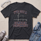 A black graphic t-shirt laid flat on a textured beige fabric background, styled with safety goggles, gray sneakers, and a denim jacket. The t-shirt features a graphic of a complex number plot with the text 'I'VE GOT A COMPLEX PERSONALITY' in red and blue outlined lettering.