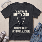 A black graphic t-shirt laid flat on a beige fabric background, surrounded by styling props including clear safety goggles, gray sneakers, and a denim jacket. The t-shirt features a white printed graphic of a parabola with the text 'I'M HAVING AN IDENTITY CRISIS BECAUSE MY LIFE HAS NO REAL ROOTS'.