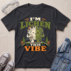 A black science t-shirt featuring a cute lichen character with the pun “I’m Lichen This Vibe,” surrounded by retro botanical and nature-inspired accents.