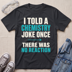 A black graphic t-shirt laid flat on a light beige textured background, surrounded by styling props including safety goggles, gray sneakers, and a denim jacket. The t-shirt features the text 'I TOLD A CHEMISTRY JOKE ONCE THERE WAS NO REACTION' in white and bright teal lettering.