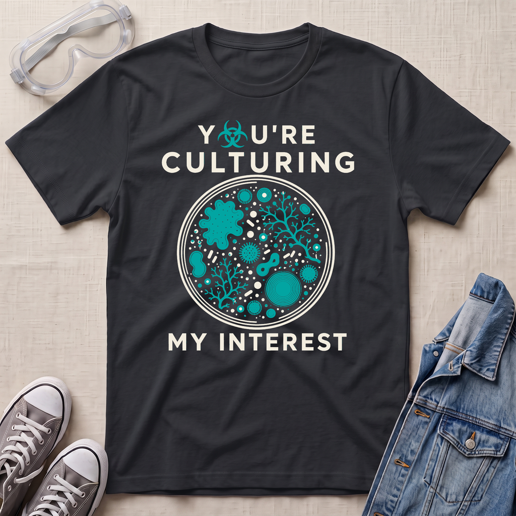A black graphic t-shirt laid flat on a light beige textured background, surrounded by styling props including safety goggles, gray sneakers, and a denim jacket. The t-shirt features a circular petri-dish graphic filled with teal microorganisms and white text that reads 'YOU'RE CULTURING MY INTEREST'.