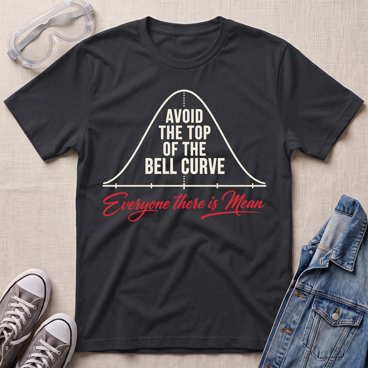 A black graphic t-shirt laid flat on a light beige textured background, styled with safety goggles, gray sneakers, and a denim jacket. The t-shirt features a white bell curve graphic with the text 'AVOID THE TOP OF THE BELL CURVE' and red script text reading 'Everyone there is Mean'.