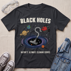 A black graphic t-shirt laid flat on a textured fabric background, styled with safety goggles, sneakers, and a denim jacket. The t-shirt features a cartoon illustration of a vacuum cleaner falling into a black hole surrounded by planets, with the text 'BLACK HOLES' and 'NATURE'S ULTIMATE CLEANING SERVICE'.