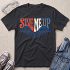 A black graphic t-shirt laid flat on a light beige textured background, styled with safety goggles, gray sneakers, and a denim jacket. The t-shirt features a retro-style graphic reading 'SINE ME UP' in red, white, and blue, with a blue wave design underneath.
