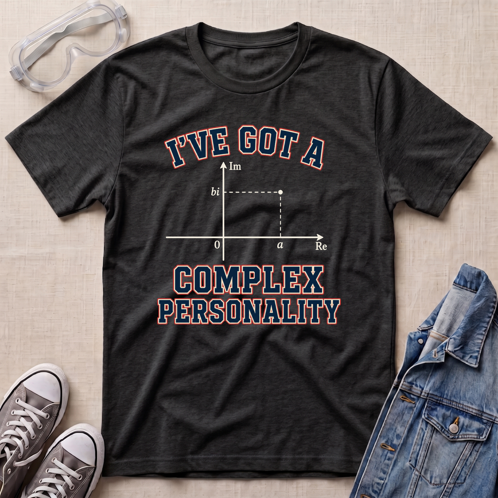 A dark heather gray graphic t-shirt laid flat on a beige fabric background, styled with safety goggles, gray sneakers, and a denim jacket. The t-shirt features a graphic of a complex impedance plot with the text 'I'VE GOT A COMPLEX PERSONALITY' in navy blue with a red outline.