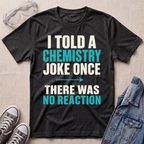 A dark heather gray graphic t-shirt laid flat on a beige textured background, surrounded by styling props including safety goggles, gray sneakers, and a denim jacket. The t-shirt features a bold text design in white and teal reading 'I TOLD A CHEMISTRY JOKE ONCE THERE WAS NO REACTION'.