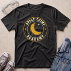 A dark heather gray graphic t-shirt laid flat on a beige textured background, styled with safety goggles, gray sneakers, and a denim jacket. The t-shirt features a circular graphic with a yellow banana and stars reading 'SPACE CHIMP ACADEMY'.