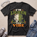 A dark heather grey science t-shirt featuring a cute lichen character with the pun “I’m Lichen This Vibe,” surrounded by retro botanical and nature-inspired accents.