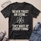 A dark heather gray graphic t-shirt with white text reading 'NEVER TRUST AN ATOM.' and 'THEY MAKE UP EVERYTHING' with an image of an atom in between the texts.