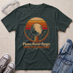 A dark green graphic t-shirt laid flat on a light beige fabric background, styled with safety goggles, gray sneakers, and a denim jacket. The t-shirt features a retro circular graphic of Pluto with the text 'Pluto: Never Forget 1930-2006'.