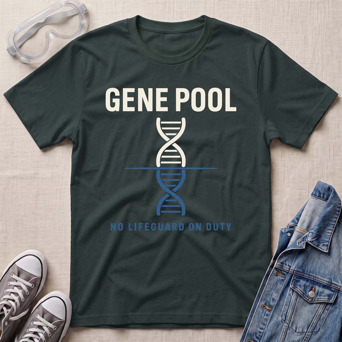 A forest green graphic t-shirt laid flat on a light beige textured background, surrounded by lifestyle props including safety goggles, gray sneakers, and a denim jacket. The t-shirt features a white and blue DNA double helix graphic with the text 'GENE POOL' and 'NO LIFEGUARD ON DUTY'.