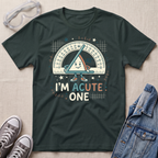 A dark green graphic t-shirt laid flat on a light beige textured background, styled with safety glasses, gray sneakers, and a denim jacket. The t-shirt features a cartoon triangle protractor character and the text 'I'M ACUTE ONE.