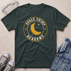 A dark forest green crewneck t-shirt with a 'Space Chimp Academy' graphic featuring a yellow banana and stars, styled in a flat lay with safety goggles, gray sneakers, and a denim jacket on a beige fabric background.