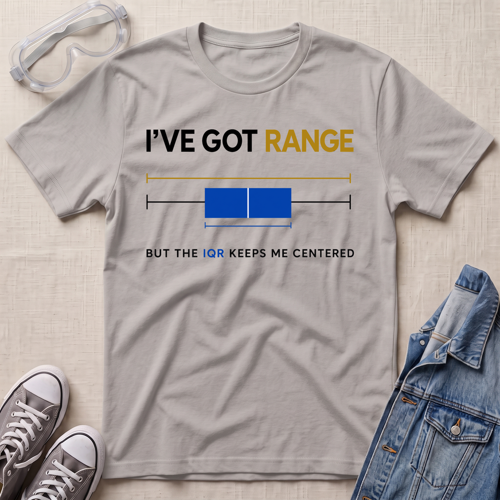 A light gray graphic t-shirt laid flat on a textured beige surface, styled with safety goggles, gray sneakers, and a denim jacket. The t-shirt features a humorous graphic with the text 'I'VE GOT RANGE BUT THE IQR KEEPS ME CENTERED' and a blue box plot illustration.