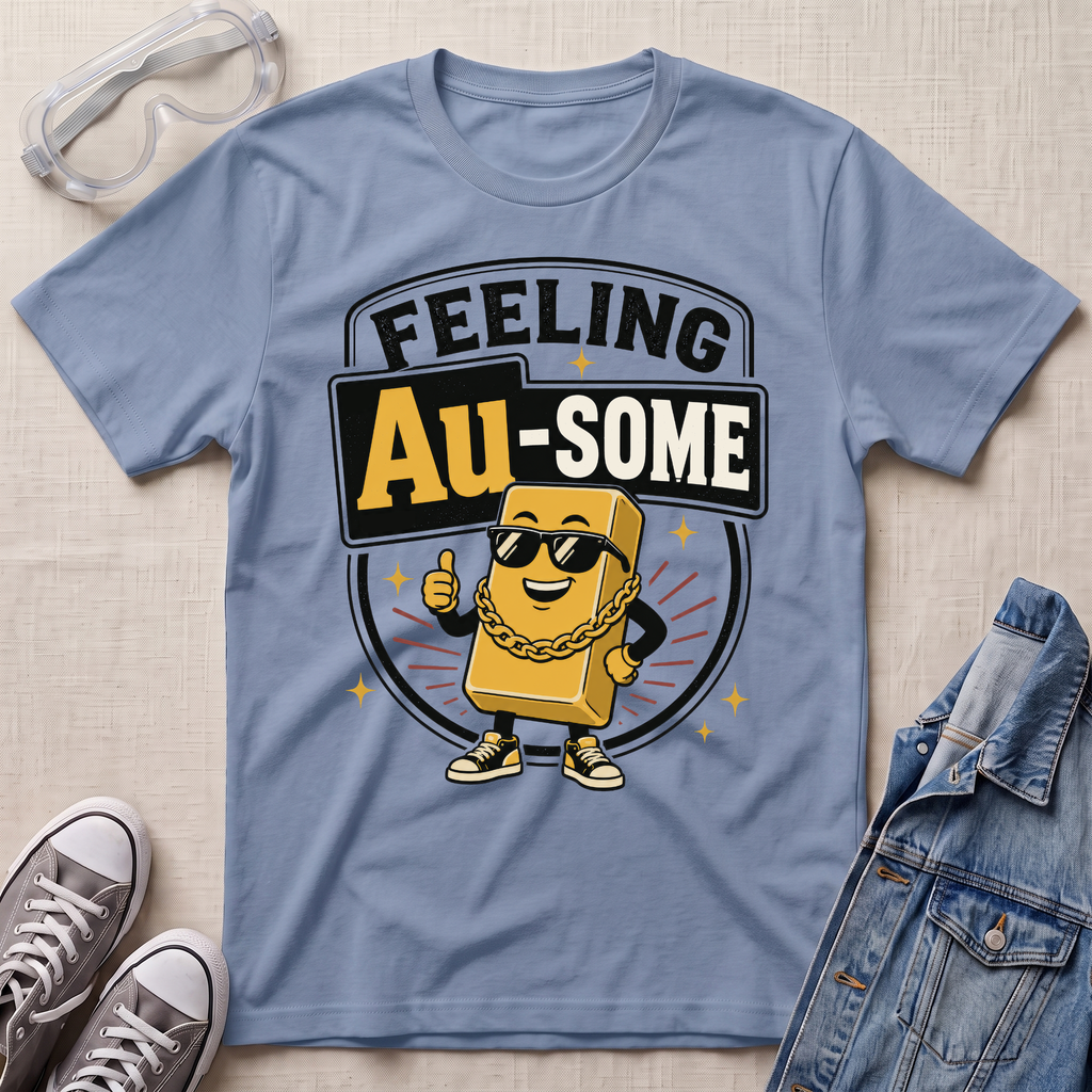 A light blue graphic t-shirt laid flat on a beige textured background, styled with safety goggles, gray sneakers, and a denim jacket. The t-shirt features a cartoon gold bar character wearing sunglasses and a gold chain, with the text 'FEELING Au-SOME' in a circular badge design.