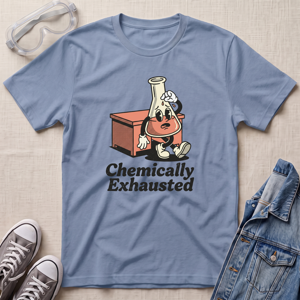 A light blue crewneck t-shirt laid flat on a beige textured background, styled with safety goggles, gray sneakers, and a denim jacket. The t-shirt features a cartoon graphic of a lab flask character with sunglasses and a sweatshirt, sitting next to a beaker, with the text 'Chemically Exhausted' printed below.