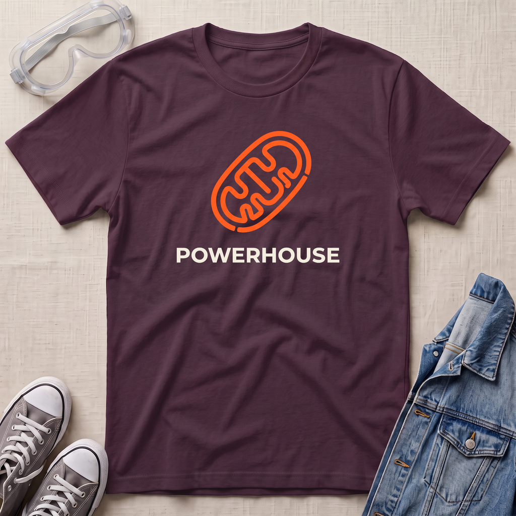 A dark plum purple t-shirt with an orange mitochondrial outline and the word 'POWERHOUSE' printed in white. The shirt is displayed in a flat-lay arrangement on a beige fabric background, surrounded by props including safety goggles, gray sneakers, and a blue denim jacket.