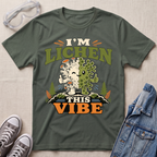 A military green science t-shirt featuring a cute lichen character with the pun “I’m Lichen This Vibe,” surrounded by retro botanical and nature-inspired accents.