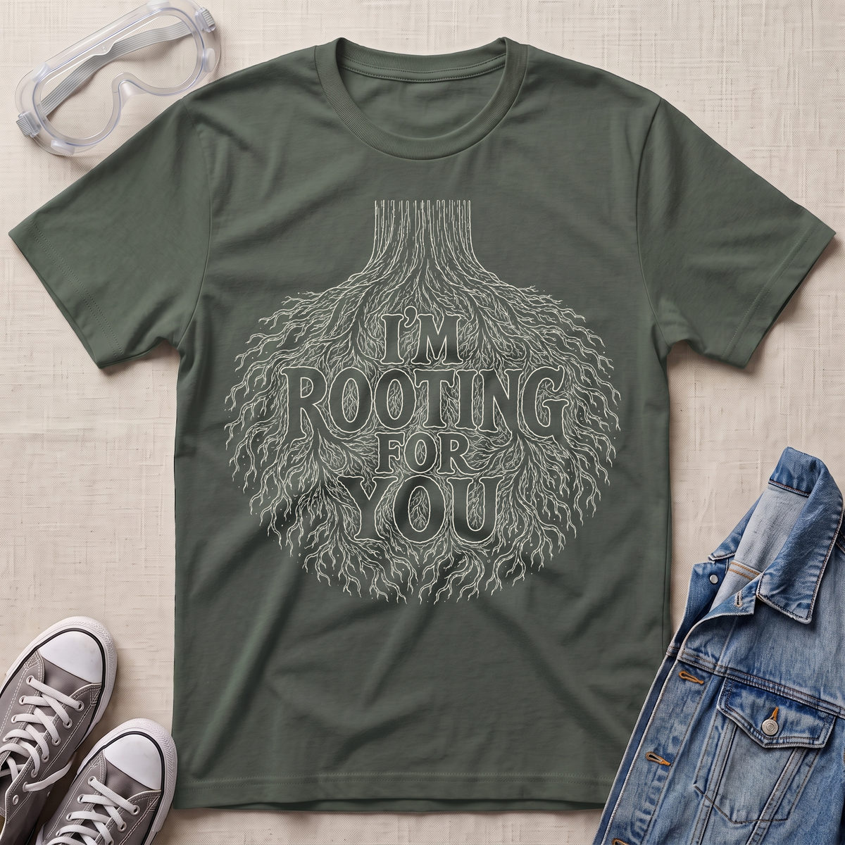 A military green botanical t-shirt featuring an intricate tree root illustration with the pun “I’m Rooting For You” in bold vintage-style lettering.
