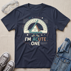 A navy blue graphic t-shirt laid flat on a beige fabric background, styled with safety glasses, gray sneakers, and a denim jacket. The t-shirt features a cartoon triangle protractor character and the text 'I'M ACUTE ONE.