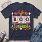 A navy blue graphic t-shirt laid flat on a light beige fabric background, styled with clear safety goggles, gray sneakers, and a denim jacket. The t-shirt features a colorful Halloween-themed graphic reading 'THE ELEMENTS OF BOO SURPRISE' with periodic-table-style elements, ghosts, pumpkins, bats, and a skull.