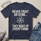 A navy blue graphic t-shirt with white text reading 'NEVER TRUST AN ATOM.' and 'THEY MAKE UP EVERYTHING' with an image of an atom in between the texts.