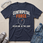 A navy blue graphic t-shirt laid flat on a beige fabric background, styled with safety goggles, gray sneakers, and a denim jacket. The t-shirt features the text 'CENTRIPETAL FORCE' in white and orange, with a circular diagram graphic below it and the phrase 'KEEPS ME IN THE LOOP'.