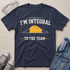 A navy blue graphic t-shirt laid flat on a beige fabric background, styled with safety goggles, gray sneakers, and a denim jacket. The t-shirt features a white graphic that reads 'I'M INTEGRAL TO THE TEAM' with a yellow integral curve diagram.