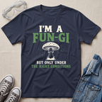A navy blue graphic t-shirt laid flat on a beige fabric background, styled with safety goggles, gray sneakers, and a denim jacket. The t-shirt features a white mushroom illustration and the text 'I'M A FUN-GI BUT ONLY UNDER THE RIGHT CONDITIONS' in white and green.