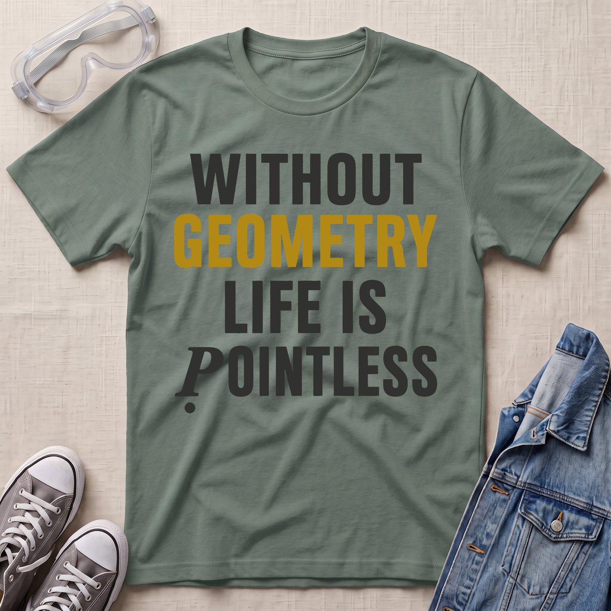 An olive green graphic t-shirt laid flat on a light beige textured background, surrounded by styling props including clear safety goggles, gray sneakers, and a blue denim jacket. The t-shirt features the text 'WITHOUT GEOMETRY LIFE IS POINTLESS' in dark gray and mustard yellow lettering.