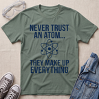 A olive green graphic t-shirt with white text reading 'NEVER TRUST AN ATOM.' and 'THEY MAKE UP EVERYTHING' with an image of an atom in between the texts.