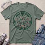 A sage green graphic t-shirt featuring a circular 'Cell Division Social Club' design with cartoon cells and microscopes, styled in a flat lay with safety goggles, sneakers, and a denim jacket on a textured beige background.