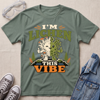 A sage green science t-shirt featuring a cute lichen character with the pun “I’m Lichen This Vibe,” surrounded by retro botanical and nature-inspired accents.