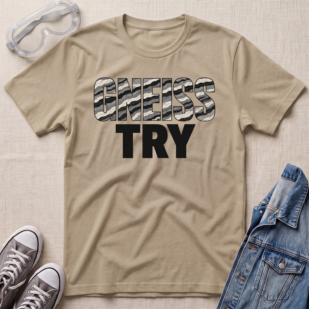 A beige graphic t-shirt laid flat on a textured light beige background, styled with safety goggles, gray sneakers, and a blue denim jacket. The t-shirt features the text 'GNEISS TRY' with 'GNEISS' filled with a black and white camouflage pattern and 'TRY' in solid black below it.