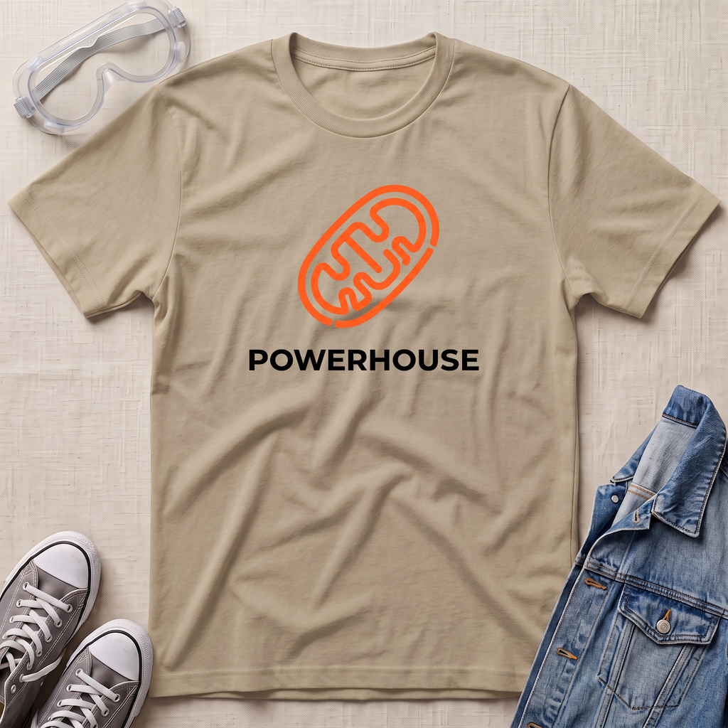 A beige short-sleeve t-shirt with an orange mitochondrion graphic and the word 'POWERHOUSE' printed in black, styled in a flat lay with safety goggles, gray sneakers, a denim jacket, and a textured fabric background.