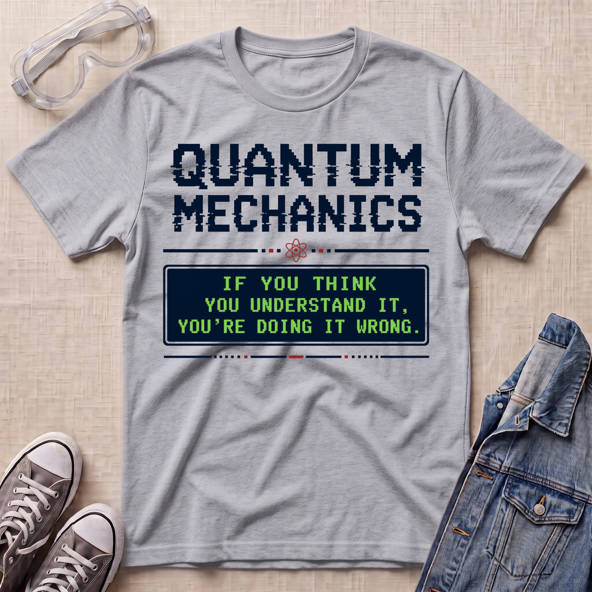 A light gray graphic t-shirt featuring a retro computer-style text message that reads 'QUANTUM MECHANICS' and 'IF YOU THINK YOU UNDERSTAND IT, YOU'RE DOING IT WRONG.' in dark blue and neon green.
