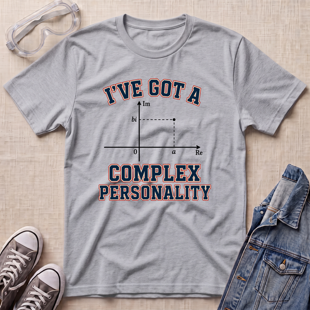 A heather gray graphic t-shirt laid flat on a beige textured surface, styled with safety goggles, gray sneakers, and a denim jacket. The t-shirt features a graphic of a complex plane with the text 'I'VE GOT A COMPLEX PERSONALITY' in navy blue with a red outline.