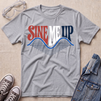 A heather gray short-sleeve t-shirt with a retro graphic reading 'SINE ME UP' in red, white, and navy, styled in a flat lay with safety glasses, gray sneakers, and a denim jacket on a beige textured background.