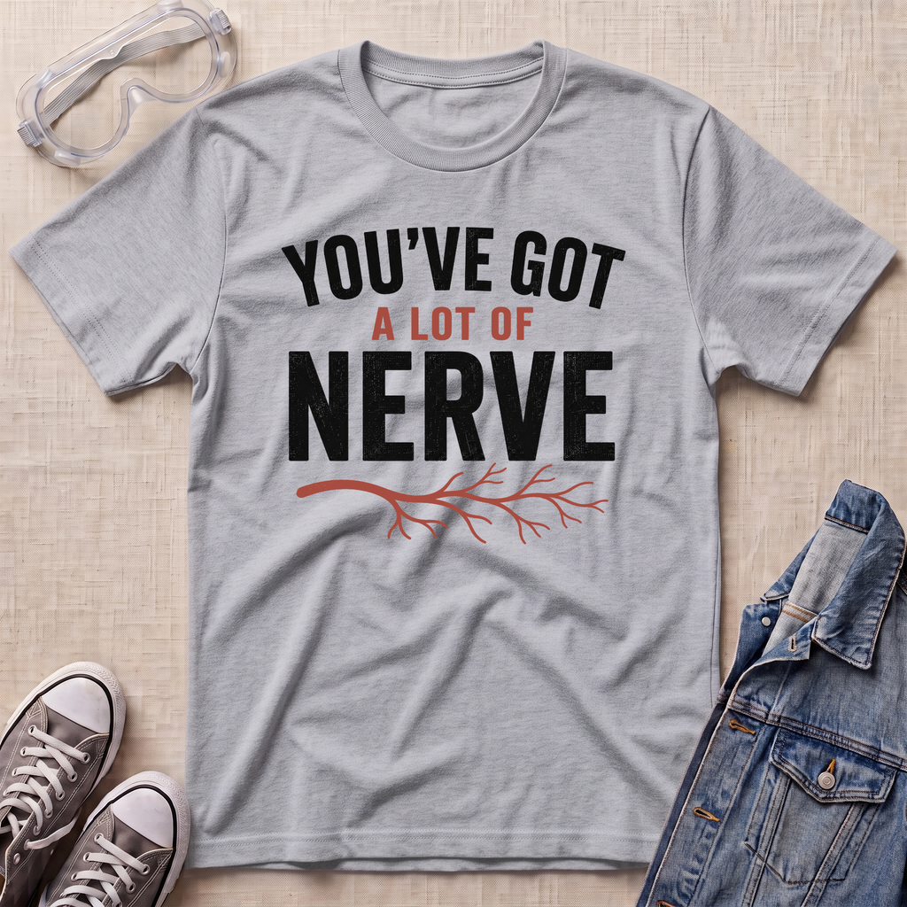 A heather gray graphic t-shirt laid flat on a light wood background, surrounded by styling props including safety glasses, a pair of gray sneakers, and a denim jacket. The t-shirt features the text 'YOU'VE GOT A LOT OF NERVE' in black and red lettering with a red branch graphic underneath.