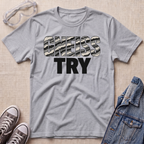 A heather gray short-sleeve t-shirt with the text 'GNEISS TRY' printed on the chest, styled in a flat lay with safety goggles, sneakers, and a denim jacket on a light beige textured background.