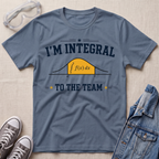 A slate blue graphic t-shirt laid flat on a light beige textured background, styled with safety goggles, gray sneakers, and a denim jacket. The t-shirt features a dark navy blue graphic that reads 'I'M INTEGRAL TO THE TEAM' with a yellow integral curve diagram in the center.