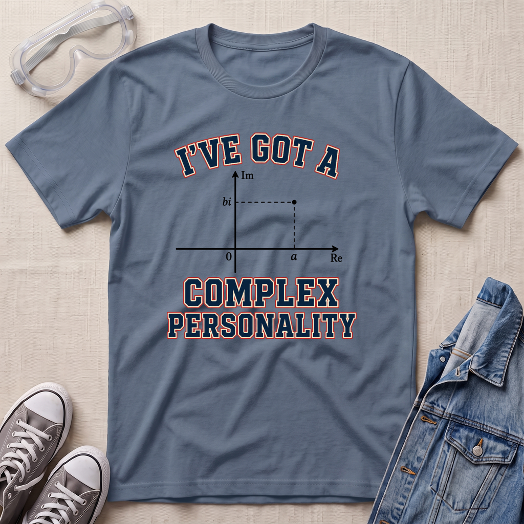 A slate blue graphic t-shirt laid flat on a beige textured background, styled with safety goggles, gray sneakers, and a denim jacket. The t-shirt features a graphic of a complex number plot with the text 'I'VE GOT A COMPLEX PERSONALITY'.