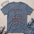 A slate blue graphic t-shirt laid flat on a beige textured background, styled with safety goggles, gray sneakers, and a denim jacket. The t-shirt features a graphic of a complex number plot with the text 'I'VE GOT A COMPLEX PERSONALITY'.